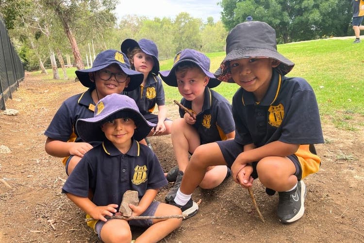 5 students playing with sticks in the dirt, smiling at the camera.