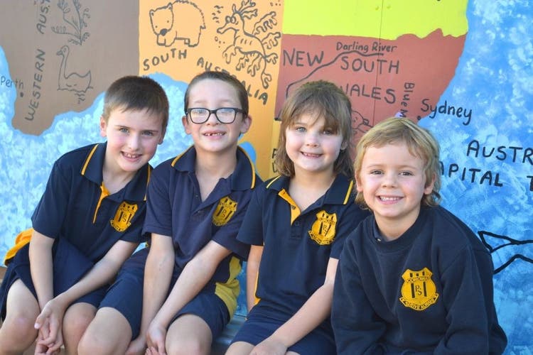 4 students smiling at the camera, sitting in front of a mural of Australia.