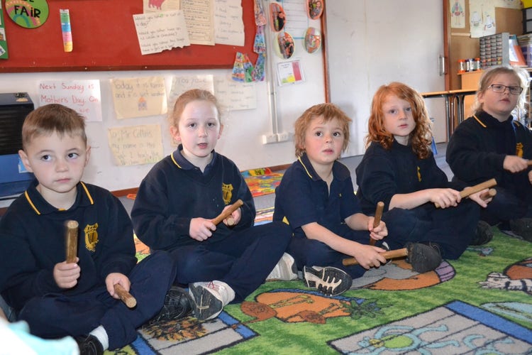 5 students sitting on the floor using clapping sticks.