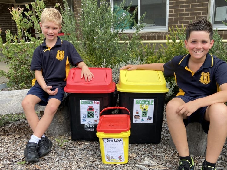 2 students sitting beside some new bins showcasing the different sorts of bins available.