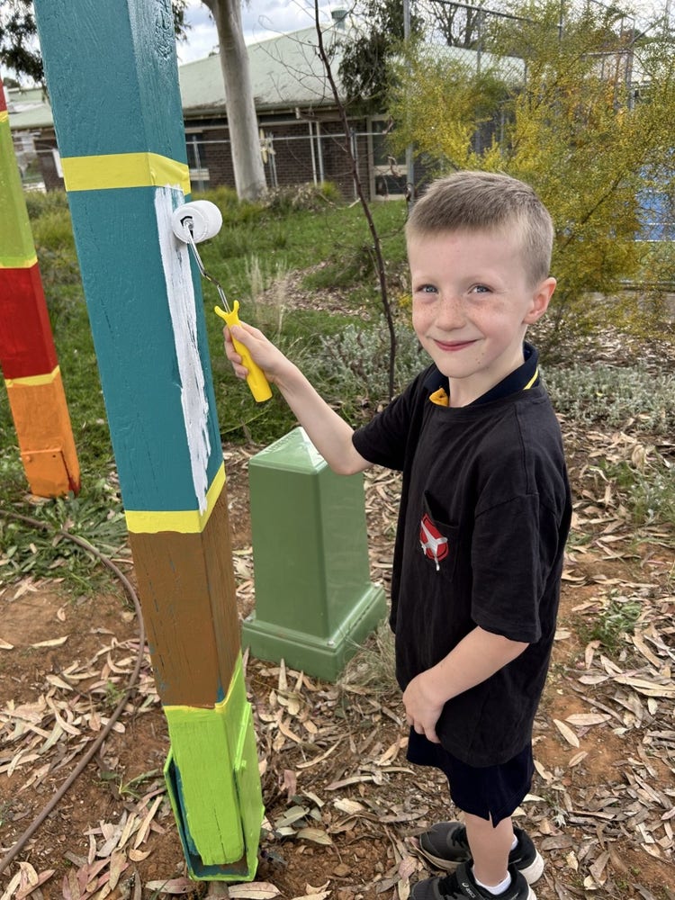 a student using a roller to paint a totem pole white.