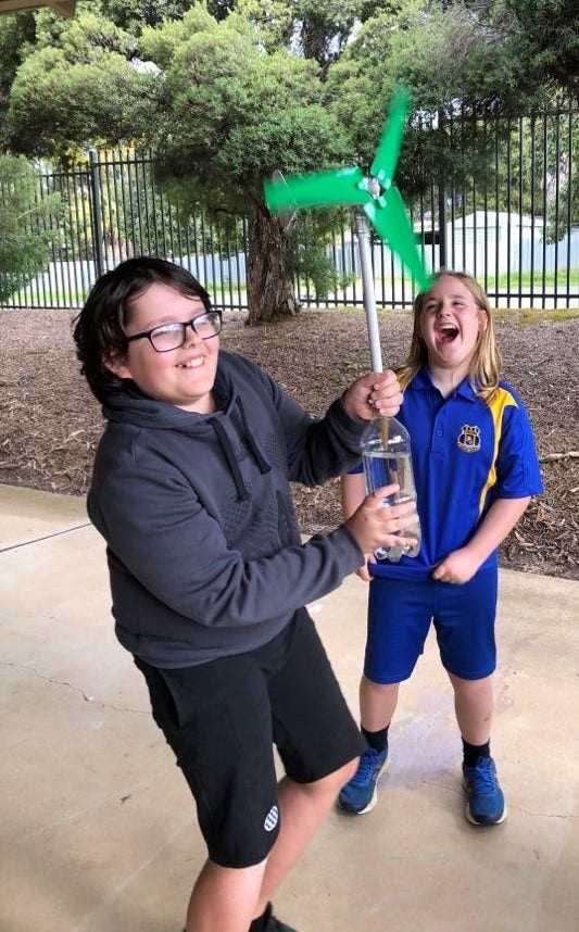 2 students smiling and laughing as they test out their wind energy experiment outside.