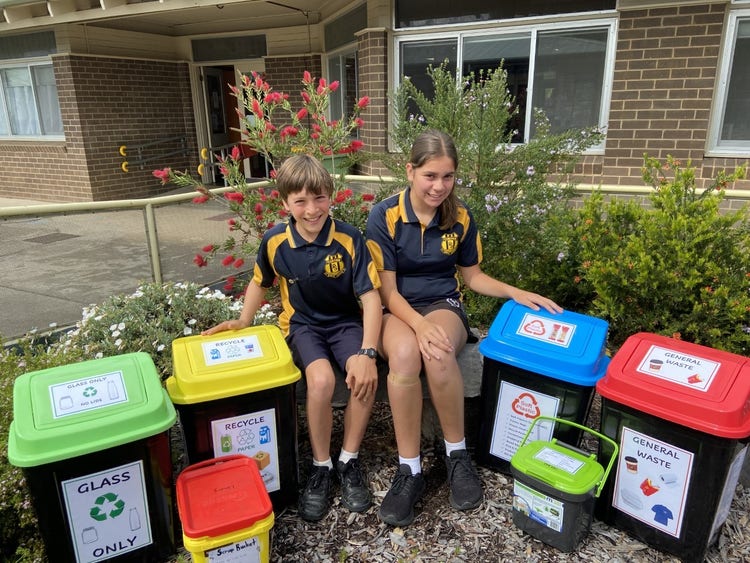 2 students sitting beside some new bins showcasing the different sorts of bins available.