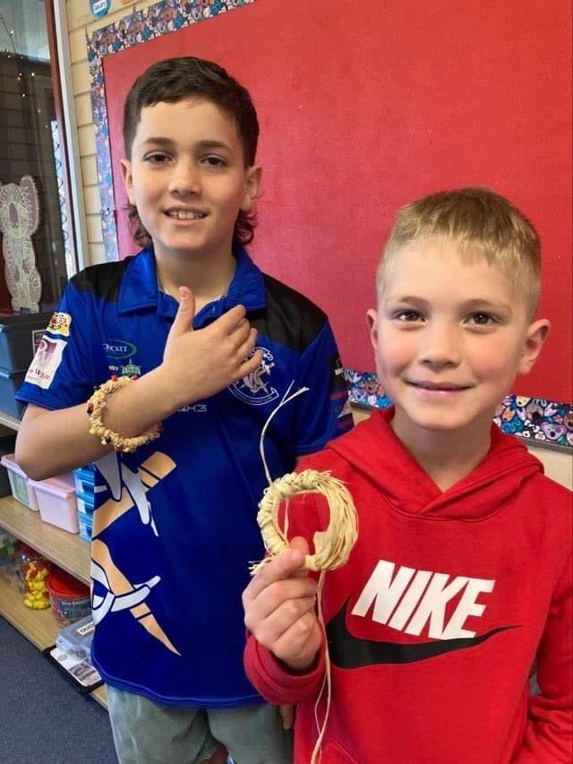 2 students showing the camera their woven raffia bracelets.