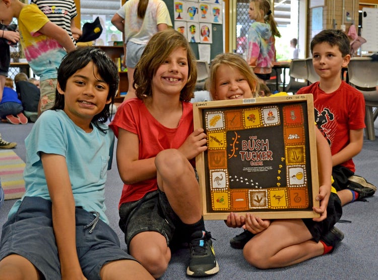 3 students holding up a square indigenous mural.