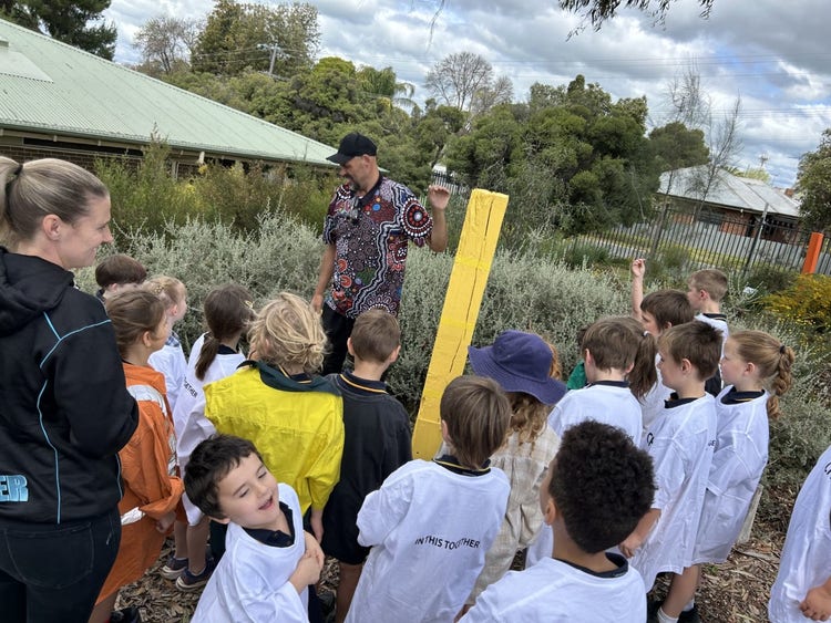 students standing around one of the indigenour totem poles listening to instructions from an indigenous artist.