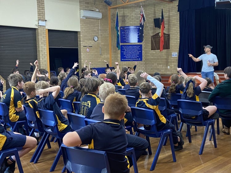 Students sitting in the hall, putting their hands up to answer questions, listening to the guest speaker.