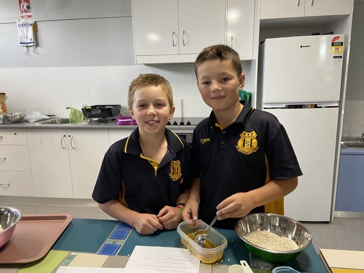 2 students cooking at the bench in the kitchen, smiling at the camera.