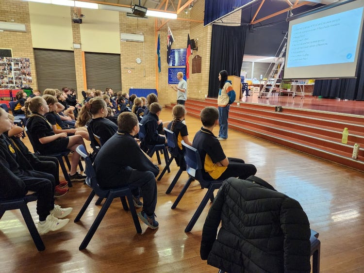 students sitting in the hall watching the presenters at the front of the hall.