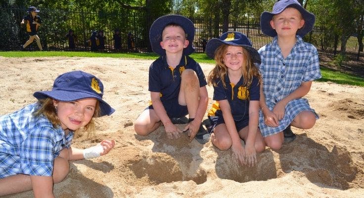 4 students playing in the sandpit with their hats on.