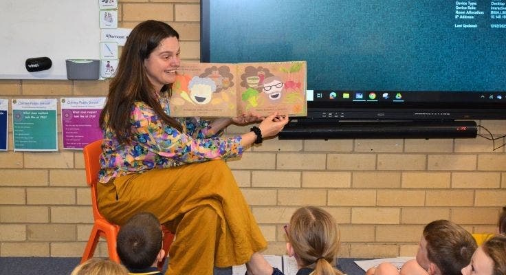 one of our teachers smiling as she reads a story to her class.