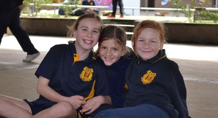 3 students sitting in a row under the cola.